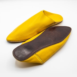 Puede incluir: Un par de zapatillas de cuero amarillo con punta puntiaguda y suela de cuero marrón.