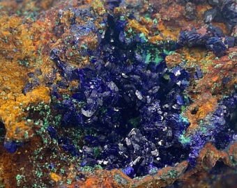 May include: A close-up of a rough, brown, orange, and green rock with a cluster of deep blue azurite crystals in the center.