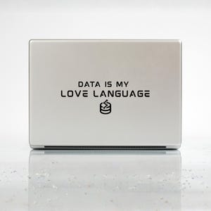 Könnte beinhalten: Ein silberner Laptop mit dem schwarzen Text "DATA IS MY LOVE LANGUAGE" und einem Datensymbol. Das Gerät steht auf einer reflektierenden Oberfläche, was auf ein modernes Design hindeutet.