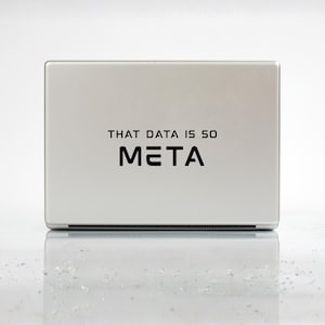 May include: A silver-colored rectangular device with the text "THAT DATA IS SO META" in black. The device is sitting on a reflective surface, and the overall aesthetic is modern and minimalist.