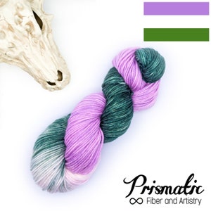 Könnte beinhalten: Ein Knäuel Garn in Lila- und Grüntönen, vor weißem Hintergrund. Das Garn ist gezwirnt und wirkt weich. Das Bild enthält auch einen weißen Schädel und den Text "Prismatic Fiber and Artistry".