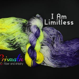 Könnte beinhalten: Zwei Garne, eines gelb und grün mit schwarzen Flecken, das andere lila und weiß mit schwarzen Flecken. Das Garn ist zu einem lockeren Knoten gebunden. Der Text "I Am Limitless" ist über dem Garn gedruckt. Der Text "Prismatic Fiber and Artistry" ist unter dem Garn gedruckt.