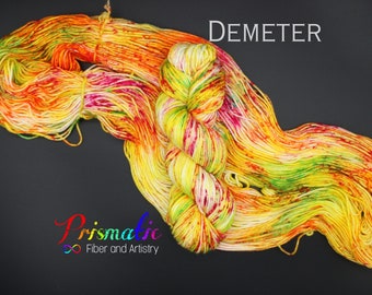 May include: A skein of yarn in a bright, colorful mix of yellow, orange, red, green, and white. The yarn is called "Demeter" and is from the brand "Prismatic Fiber and Artistry".