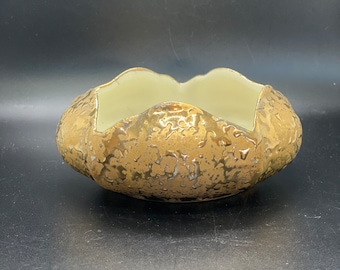 May include: A gold ceramic bowl with a textured surface. The bowl has a scalloped edge and a cream-colored interior.