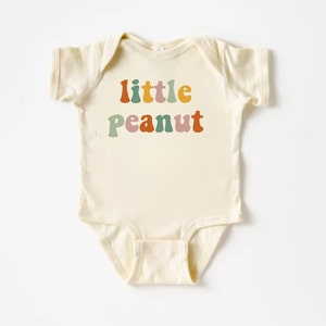 May include: A cream-colored baby onesie with the text "little peanut" in colorful retro-style lettering.