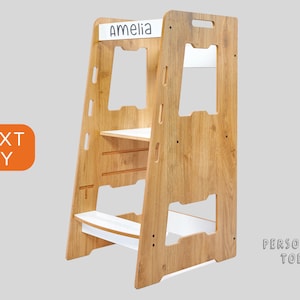 May include: A wooden step stool with a white top shelf and two white steps. The stool has a cutout for a child's feet and a handle on the top. The stool is personalized with the name "Amelia".