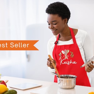 Pu&ograve; includere: Un grembiule rosso personalizzato con un design ricamato bianco di utensili da cucina e il nome "Keisha".