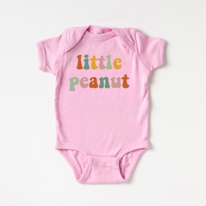 May include: Pink baby onesie with the text "little peanut" in colorful, retro-style letters.