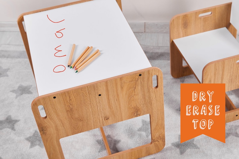 May include: A wooden children's table and chair set with a white dry erase top. The table top has red writing that says "draw" and colored pencils are on the surface. The chair also has a white dry erase top.