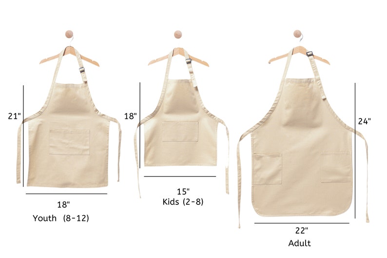 Pu&ograve; includere: Tre grembiuli in cotone beige di diverse dimensioni, appesi a grucce di legno. I grembiuli hanno una sola tasca e lacci regolabili. Le taglie sono indicate come Giovani (8-12), Bambini (2-8) e Adulti, con le misure corrispondenti in pollici.