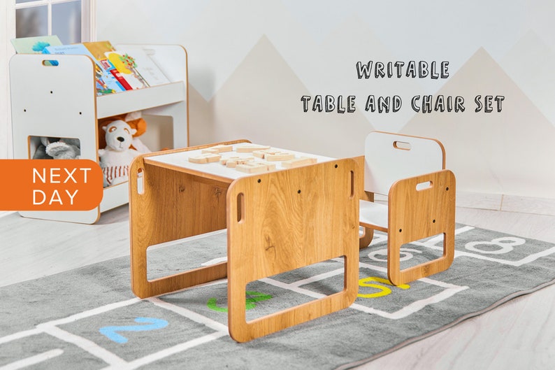 May include: A white and wood children's table and chair set with a white top that can be written on. The set is on a gray rug with numbers printed on it. The text "WRITEABLE TABLE AND CHAIR SET" is printed on the wall behind the set.