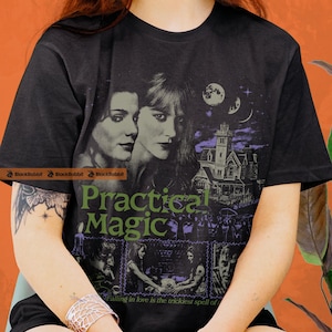 May include: Black t-shirt featuring a graphic from the movie "Practical Magic." The design includes portraits of two women, a haunted house, and the text "Practical Magic." Below the text is the phrase "Falling in love is the trickiest spell of."