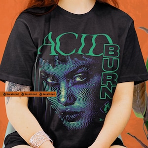Op de afbeelding: Zwart T-shirt met de tekst "ACID BURN" in groen, met een gestileerd gezicht met glitch-effect details in blauw- en paarse tinten. Het shirt heeft korte mouwen en een ronde hals.