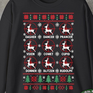 Puede incluir: Sudadera negra con un diseño navideño festivo. Presenta nombres de renos como Dasher, Dancer y Prancer, cada uno dentro de una retícula de objetivo. Incluye copos de nieve, árboles de Navidad y texto. Un logotipo circular está en la esquina inferior derecha.