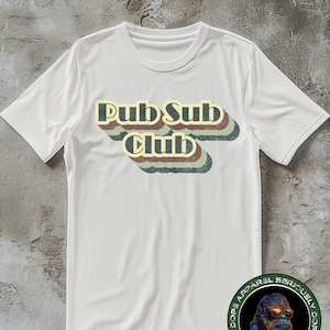 Puede incluir: Camiseta blanca con un gráfico de estilo retro que dice "Pub Sub Club" en letras coloridas y superpuestas. El gráfico tiene un aspecto vintage y descolorido.