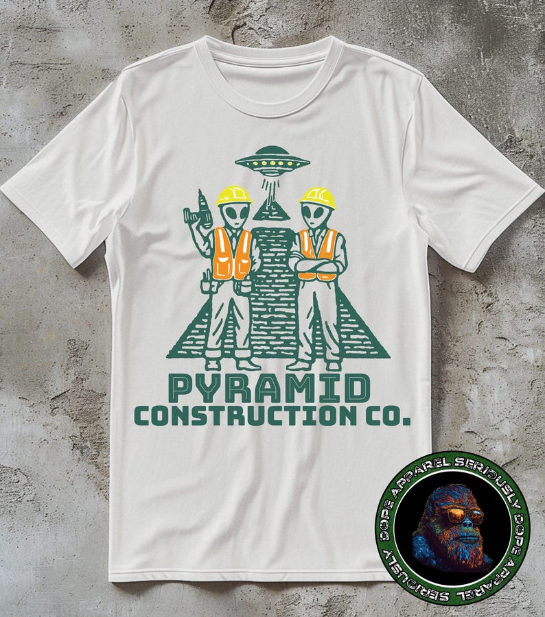 May include: White t-shirt featuring a green graphic of two alien construction workers in orange vests and yellow hard hats, standing in front of a pyramid and a UFO. The text "PYRAMID CONSTRUCTION CO." is below the graphic.