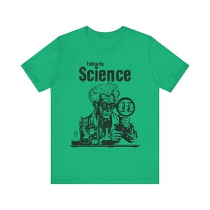 Puede incluir: Camiseta verde con una ilustraci&oacute;n en blanco y negro de un cient&iacute;fico mirando a trav&eacute;s de una lupa un billete de d&oacute;lar. El texto "Follow the Science" est&aacute; impreso sobre la ilustraci&oacute;n.