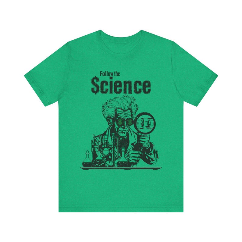 Puede incluir: Camiseta verde con una ilustraci&oacute;n en blanco y negro de un cient&iacute;fico mirando a trav&eacute;s de una lupa un billete de d&oacute;lar. El texto "Follow the Science" est&aacute; impreso sobre la ilustraci&oacute;n.