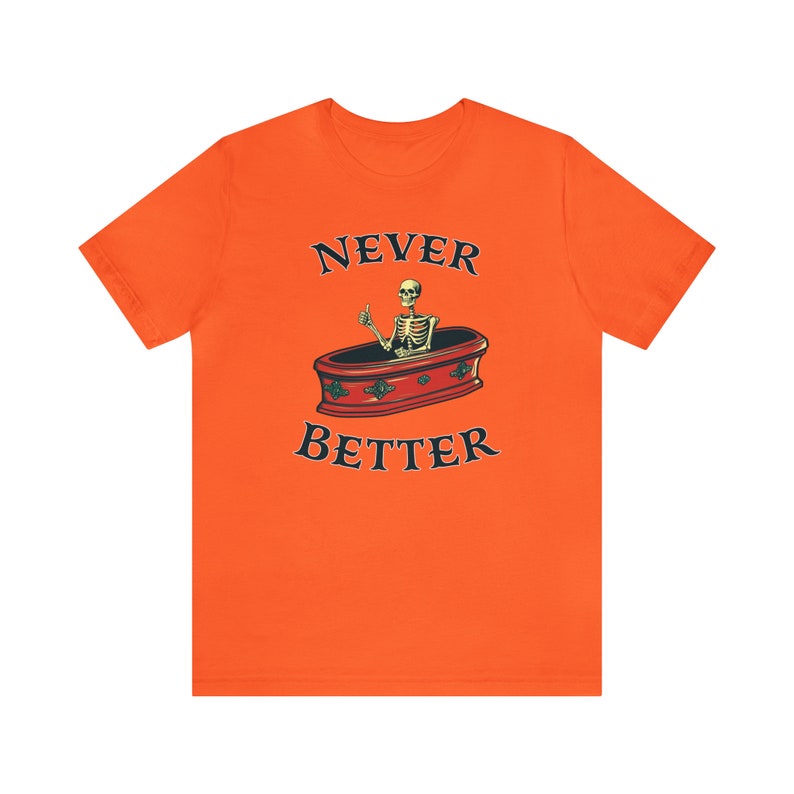 K&ouml;nnte beinhalten: Orangefarbenes T-Shirt mit dem schwarzen Text "NEVER BETTER" und einer Illustration eines Skeletts, das aus einem Sarg einen Daumen hoch zeigt. Das Design ist mittig platziert.