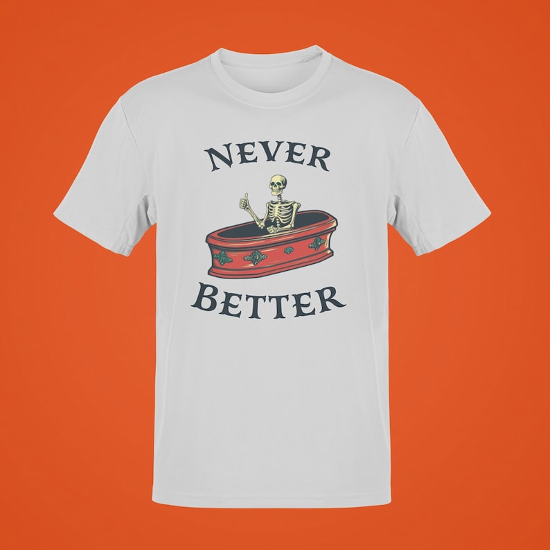 K&ouml;nnte beinhalten: Wei&szlig;es T-Shirt mit dem Text "NEVER BETTER" &uuml;ber einer Illustration eines Skeletts, das in einem Sarg einen Daumen hoch h&auml;lt. Der Sarg ist rot mit dekorativen Akzenten.