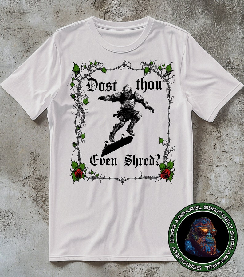 May include: White t-shirt featuring a black and white illustration of a knight skateboarding. The illustration is framed by a vine border with red roses. The text "Dost thou Even Shred?" is written in a medieval font.