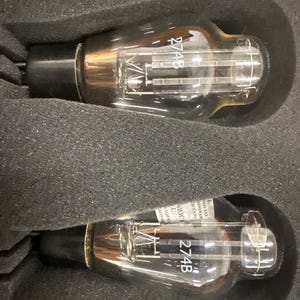 May include: Two clear glass vacuum tubes with black bases, each labeled 274B in white text. The tubes feature internal metal filaments and are securely positioned within individual molded cutouts of a dark gray foam protective storage case.