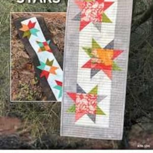 May include: A quilted table runner with a gray border and a white center, featuring large star designs in red, orange, green, and gray. The text "Desert STARS" is visible in the upper left corner. The Atkinson Designs logo is at the bottom.
