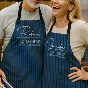 Peut inclure: Deux personnes portant des tabliers bleu marine assortis avec des rayures verticales noires. Les tabliers portent des noms et des titres de poste imprimés. L'un dit "Robert, SOUS CHEF & CIVIL ENGINEER" et l'autre dit "Jennifer, HEAD CHEF & PROJECT MANAGER".