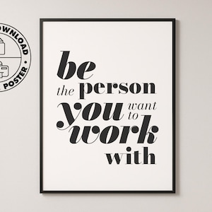 Könnte beinhalten: Ein schwarz gerahmtes Poster mit dem Text "be the person you want to work with" in einer modernen Schriftart. Das Poster hängt an einer weißen Wand in einem Büro. Ein Laptop und ein Notizblock liegen auf einem Holzschreibtisch.