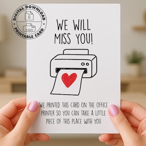 Könnte beinhalten: Eine weiße Karte mit dem Text "WE WILL MISS YOU!" und einer Zeichnung eines Druckers, der ein Papier mit einem roten Herzen druckt. Die Karte enthält auch den Text "WE PRINTED THIS CARD ON THE OFFICE PRINTER SO YOU CAN TAKE A LITTLE PIECE OF THIS PLACE WITH YOU."