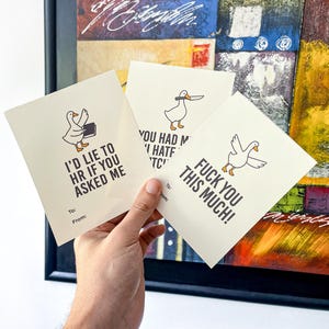 May include: Three greeting cards with a cartoon goose illustration. Each card has a different phrase: "I'd lie to HR if you asked me", "You had me at hate", and "Fuck you this much!". The cards are held in a hand.
