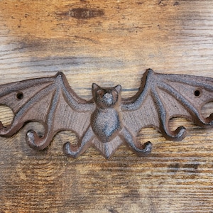 May include: A cast iron bat-shaped wall hook with five hooks. The hook is painted in a dark brown color and has a rustic finish.