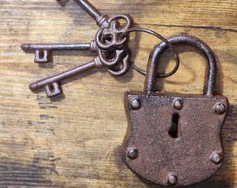 May include: A rustic, brown metal padlock with a keyhole and three matching keys on a ring. The keys have ornate designs and are connected to the padlock. The items are set against a wooden background.