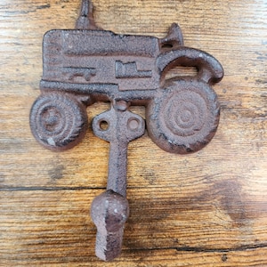 May include: A cast iron tractor shaped hook with a rustic brown finish. The hook is designed to hang items on a wall.