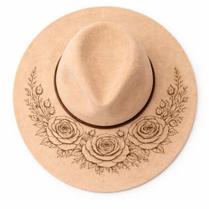 Op de afbeelding: Een beige fedora-hoed met een bruine leren band en een bloemenrozenontwerp. De hoed heeft een brede rand en een gestructureerde kroon. De rozen zijn in het oppervlak van de hoed geëtst.