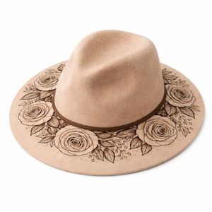 May include: A beige fedora hat with a brown leather band. The hat brim is decorated with a detailed floral design of roses and leaves in a darker beige color. The hat is set against a white background.