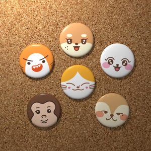 May include: A collection of six round, colorful pinback buttons with cartoon animal faces. The designs include a dog, cat, monkey, and other stylized creatures. The buttons are set against a brown corkboard background.