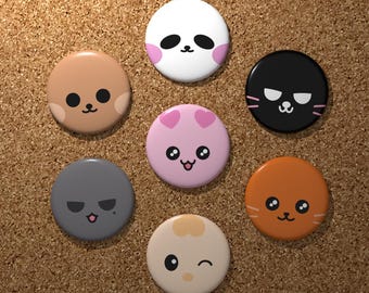 May include: A collection of seven round, colorful buttons with cartoon animal faces. The buttons feature a panda, cat, dog, and other cute characters in various colors, including white, pink, brown, gray, and orange. The buttons are arranged on a corkboard surface.