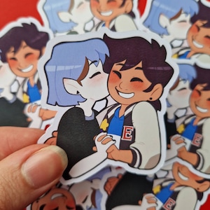 Puede incluir: Una pegatina con una pareja de dibujos animados, una persona de pelo azul con una oreja puntiaguda y una persona de pelo marrón con una chaqueta blanca y una camisa azul con una estrella y la letra 'E' en ella. La pareja se abraza y sonríe.