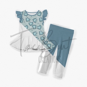 Puede incluir: Un conjunto de ropa para bebé niña con una blusa blanca con estampado de corazones azules y leggings azules con la parte inferior blanca.