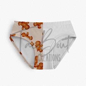 May include: White underwear with a gingerbread man pattern on the front left panel. The gingerbread men are brown with white icing details. The right panel is solid white. The text "Fab About Creations" is partially visible.