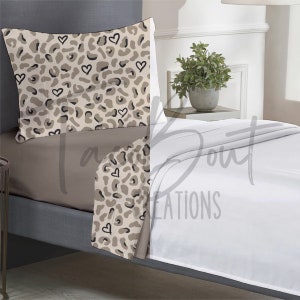 May include: A beige and brown leopard print bedding set with white hearts. The set includes a fitted sheet, flat sheet, and pillowcase.