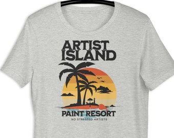 Artist Island Retreat Unisex T Shirt. The design includes a beautiful sunset over the ocean with palm trees, no stressed artists