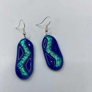 May include: A pair of blue glass earrings with a green iridescent design. The earrings are shaped like a teardrop and have silver hooks.