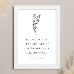 May include: A white framed print with black text and a floral illustration. The text reads "Rejoice Always, Pray Continually, Give Thanks in All Circumstances" with a Bible verse reference. The artwork features a minimalist design.