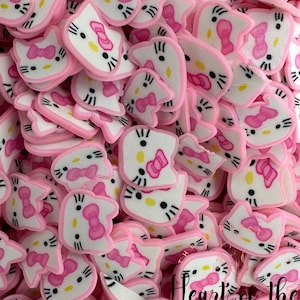 May include: A large pile of pink and white Hello Kitty-themed resin charms. Each charm features a white Hello Kitty face with black eyes, a pink bow, and a yellow nose. The charms are perfect for adding a touch of whimsy to crafts and jewelry.
