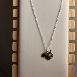 Puede incluir: Un collar de cadena de plata con un colgante de elefante de plata. El elefante tiene un coraz&oacute;n cortado de su cuerpo.