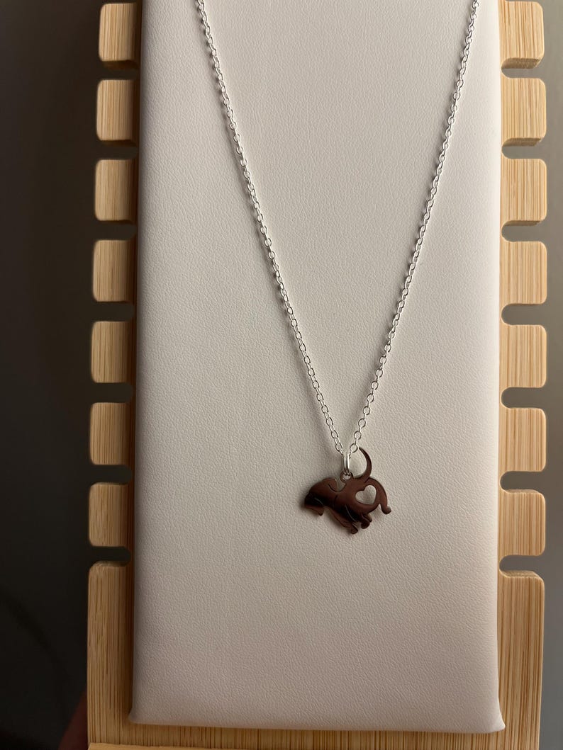 Puede incluir: Un collar de cadena de plata con un colgante de elefante de plata. El elefante tiene un coraz&oacute;n cortado de su cuerpo.