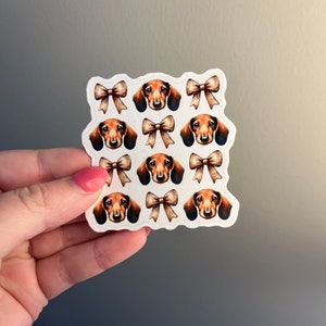 May include: A sheet of stickers featuring a repeating pattern of dachshund dog faces with brown bows. The stickers are on a white background.