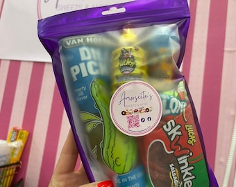 May include: A clear purple bag filled with snacks, including a pickle, a yellow bottle with the text "LUCAS", and a red package of "SKwinkles Salsaghetti". The bag has a sticker that says "Amorscita's SWEETS & MORE".